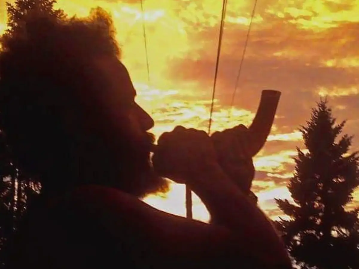 Crvne blowing a shofar with a majestic sunset in the backdrop.