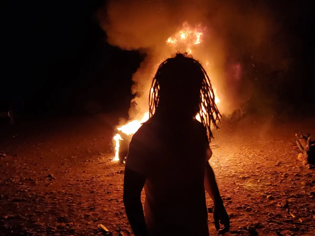 Crvne, shrouded in shadow with a huge fire burning behind him.