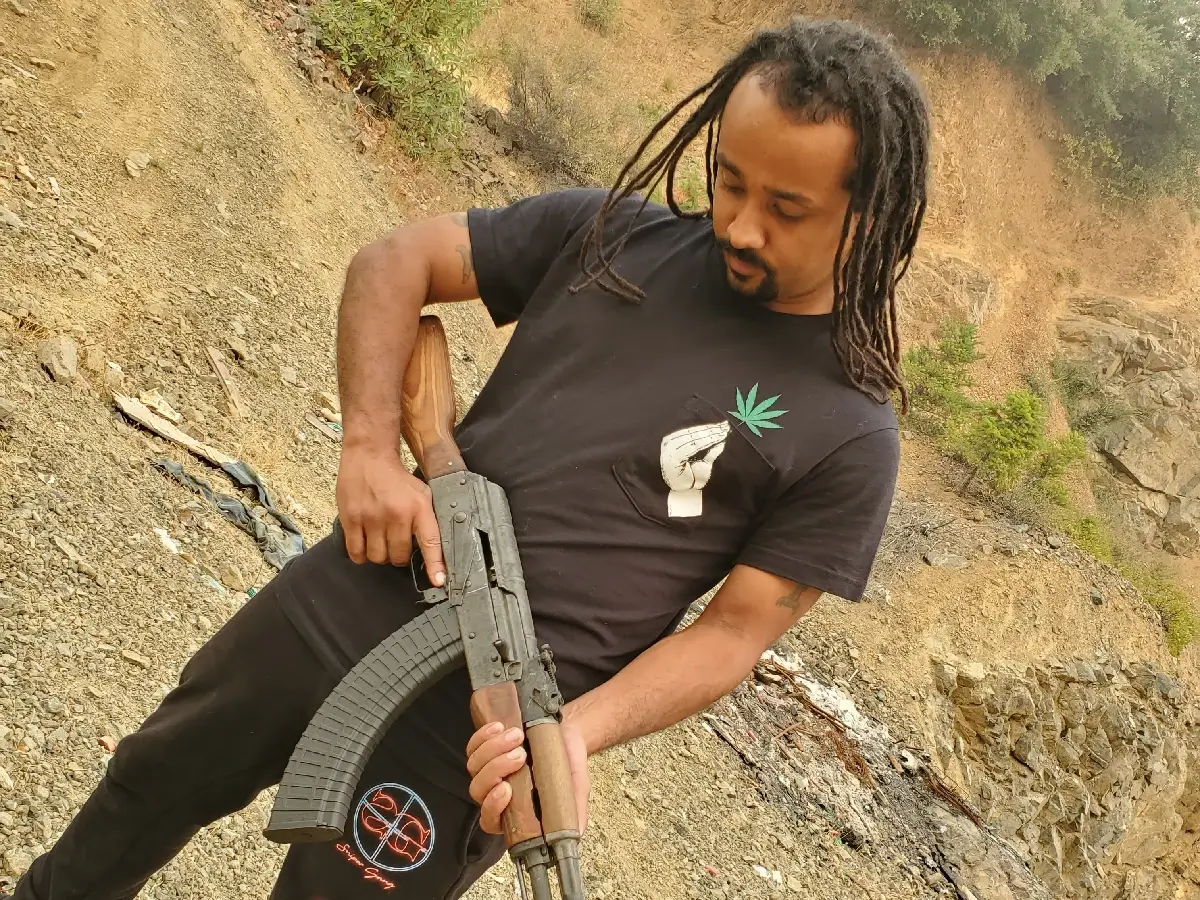 CRVNE posing, looking down at an AK-47 in his hands.